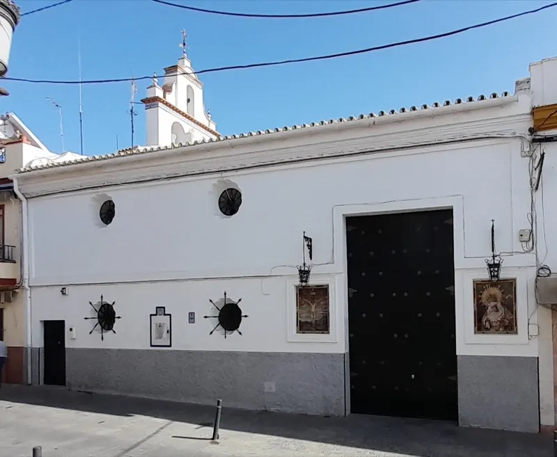 Fachada encalada de la Capilla del Rosario, con su portón negro, dos retablos cerámicos y la espadaña